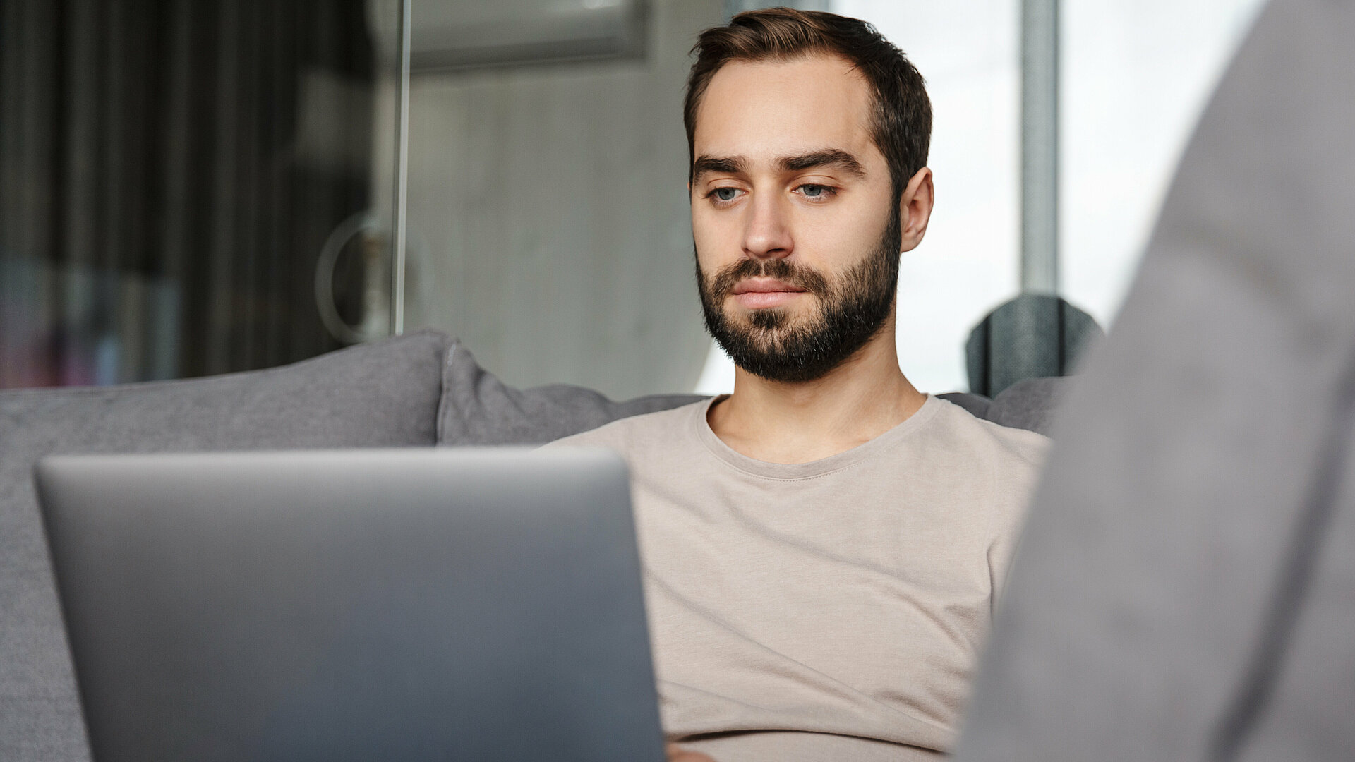 Mann sitzt mit Laptop am Sofa