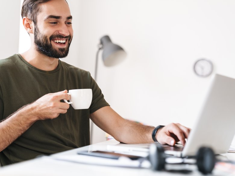 Junger Mann am Laptop und Kaffeetasse in der Hand 